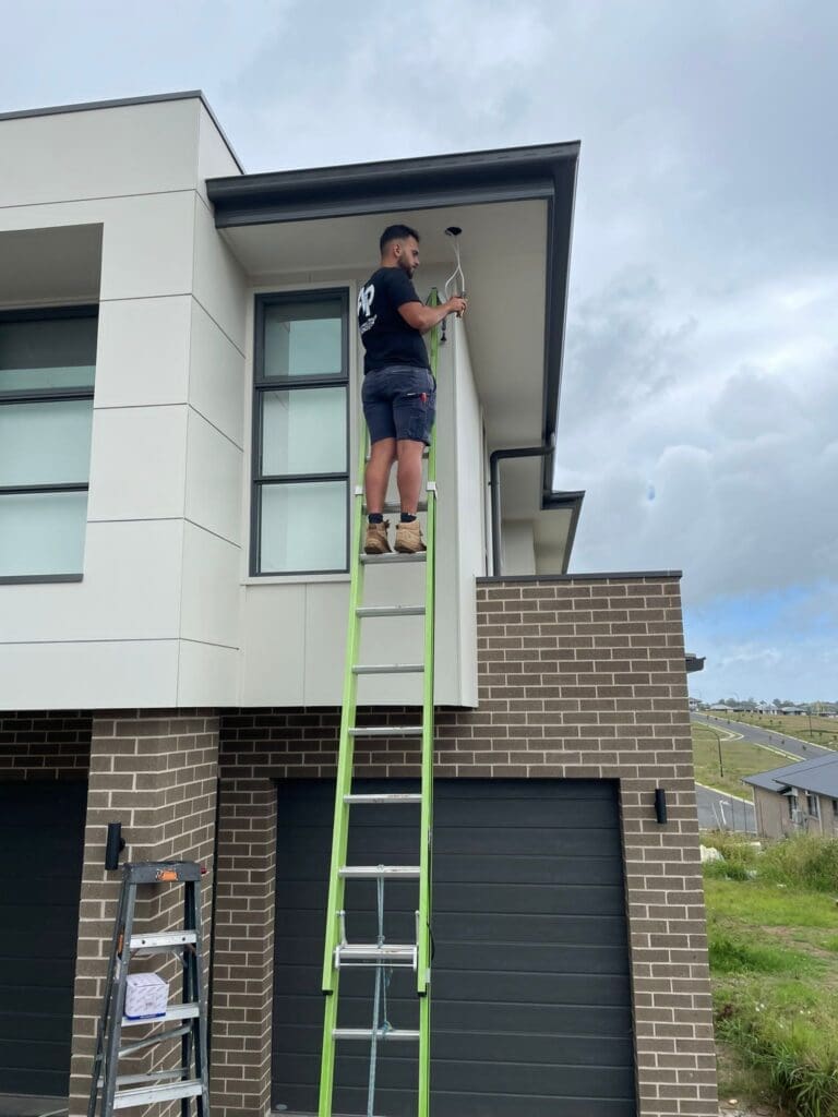 A Sydney Electrician from AP Electrical Group installing a security camera on a modern house's exterior