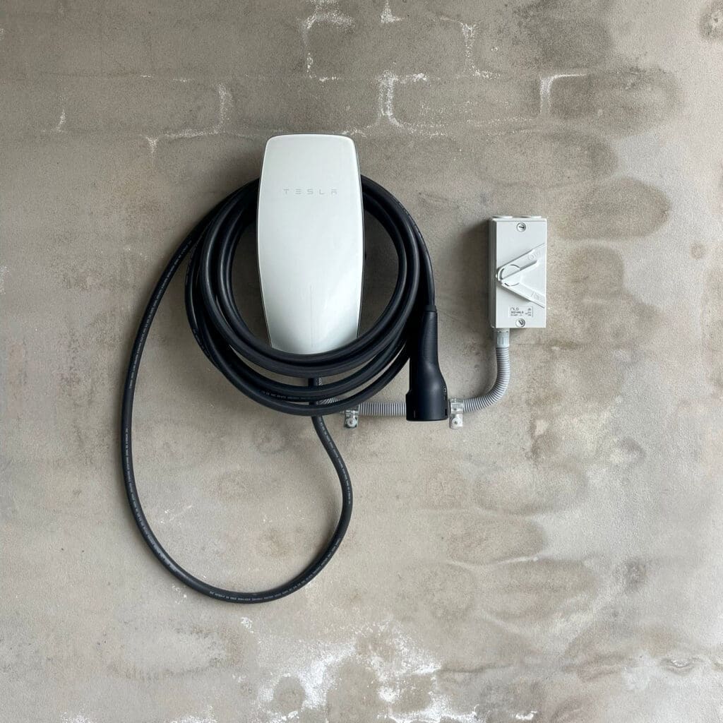 Tesla Wall Connector mounted on a textured concrete wall with coiled charging cable and safety switch