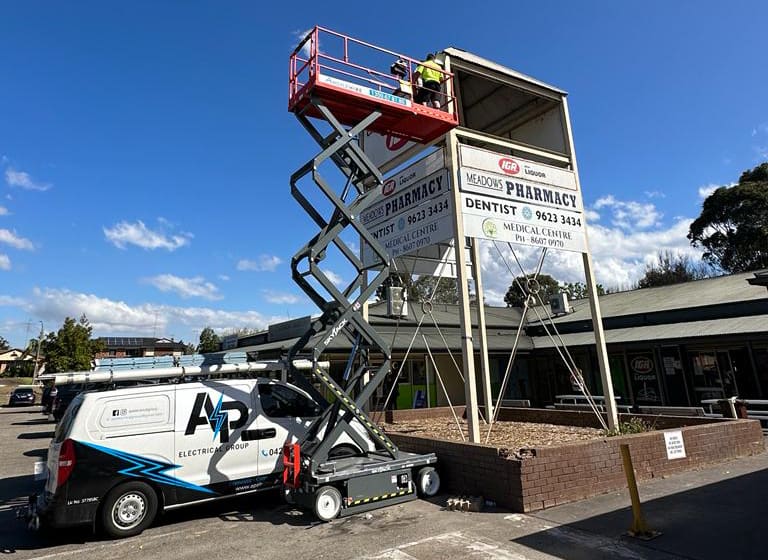 AP Electrical Group worker on scissor lift performing maintenance on commercial building signage