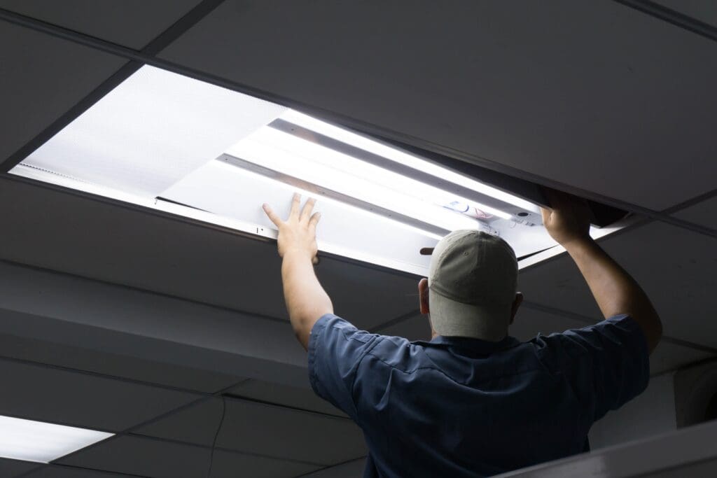 Technician installing a fluorescent light panel in a drop ceiling.