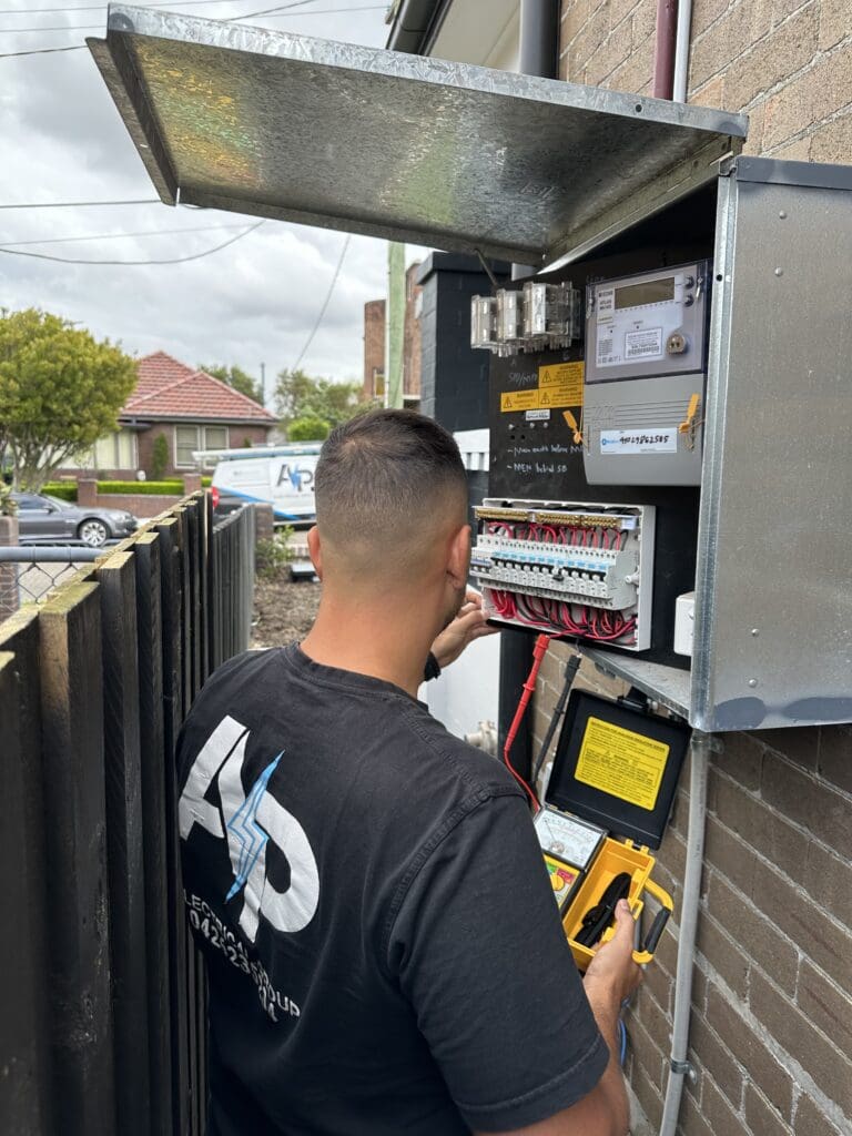 Electrician from AP Electrical Group upgrading a residential outdoor switchboard with testing equipment.