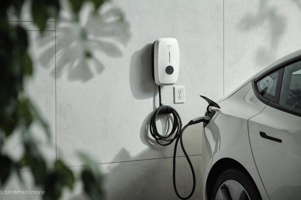 https://s.mj.run/WMxNSLMa3uI an electric car is being charged via a wall mounted white charging station. the black charging cable is coiled near the base of the charger and then extends to the car's charging port. a outlet is positioned on the light gray textured wall. the side profile of the white ev shows its charging area. blurry green leaves are visible in the foreground on the left, with leaf shadows on the wall. --chaos 5 --ar 3:2 --raw --profile tw68r83 --hd --v 8.1 Job ID: 53efe674-691f-4c18-a5b1-36107e23d97d