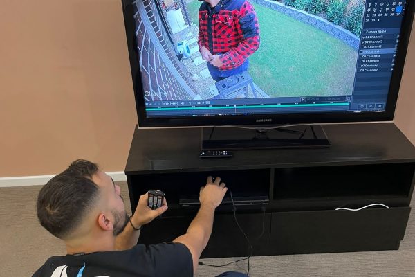 Electrician configuring a residential alarm system installation via a TV displaying security footage